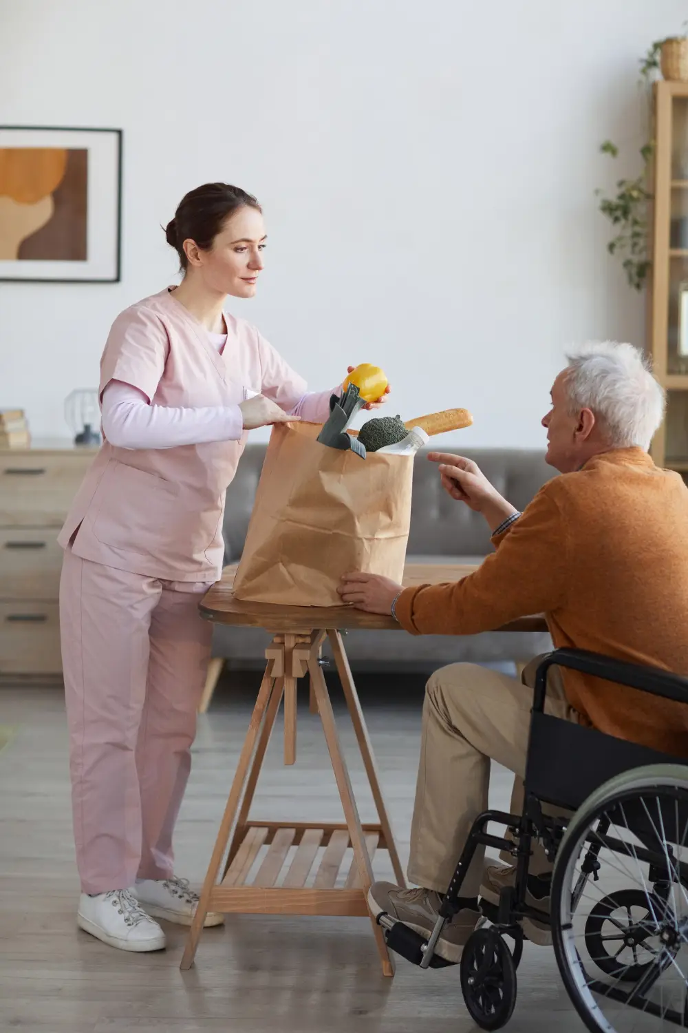 Care worker helping unpack groceries at a table for a person in a wheelchair.